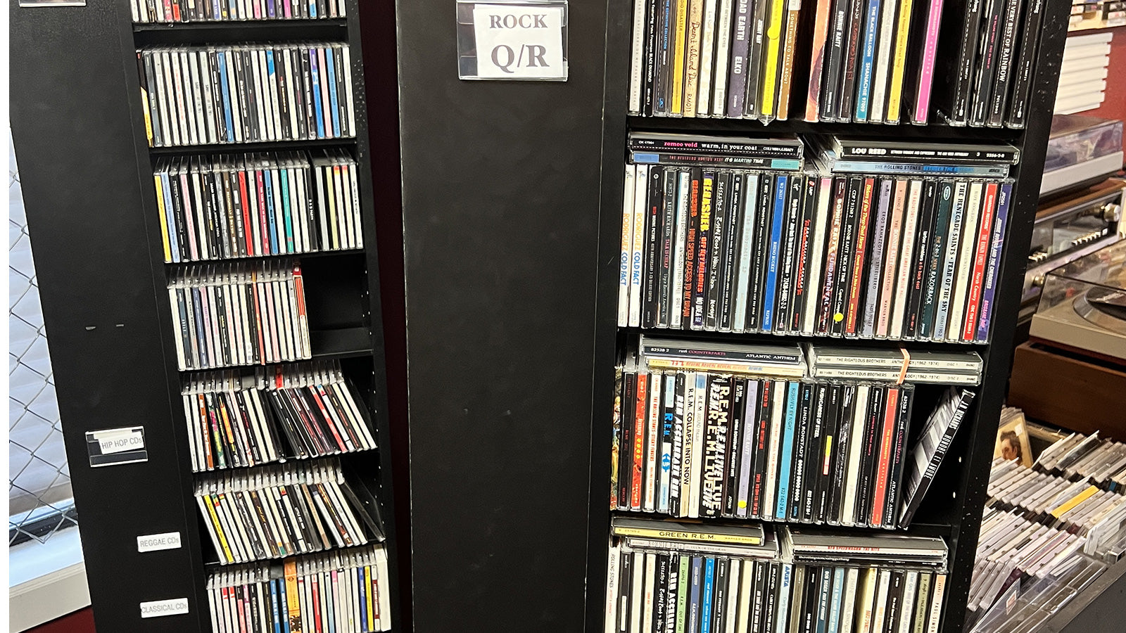 CD rack filled with CDs labeled 'Rock' and 'Q/R' on a wooden shelf at Rockin' Ruby's Records in Poulsbo, WA