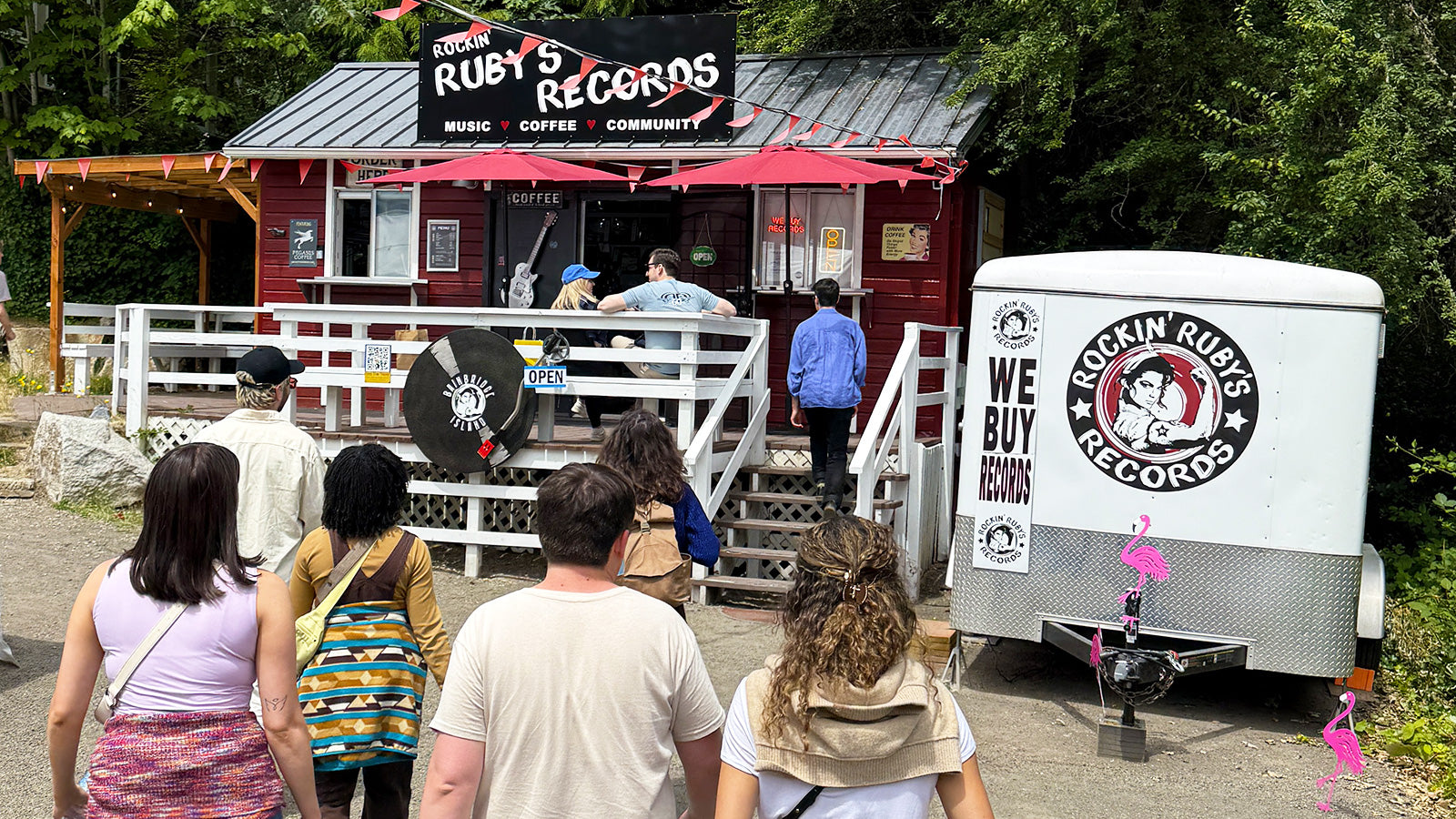 People standing outside a building with 'Ruby's Records' branding, including a trailer and people.